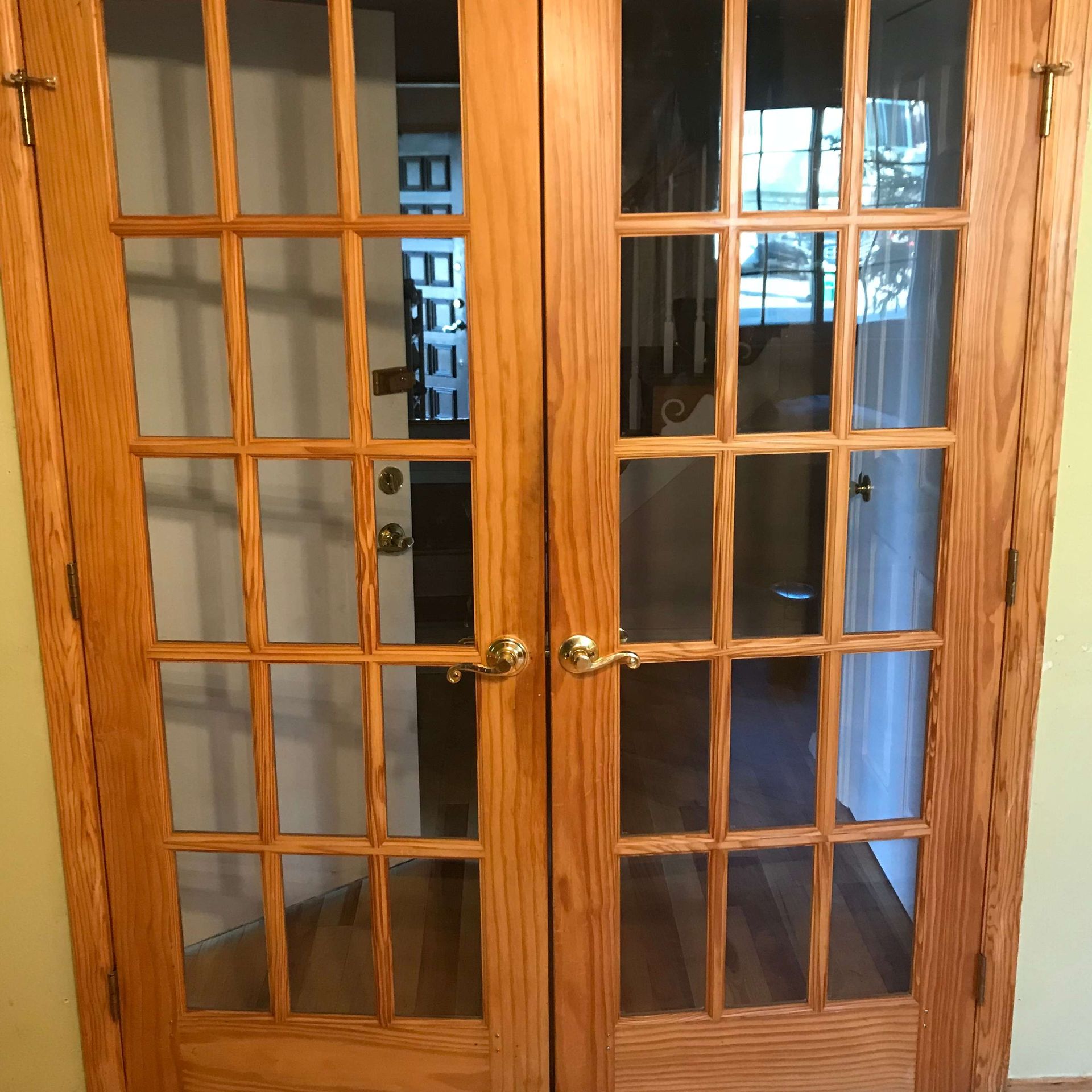 Double wooden doors with glass panes, gold handles, leading to an interior hallway.
