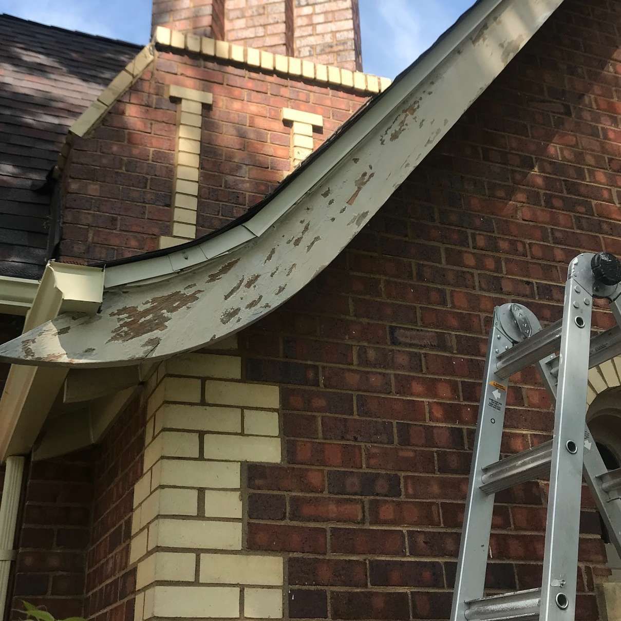 Brick building with peeling paint on a curved eave. A ladder is leaning against the wall.