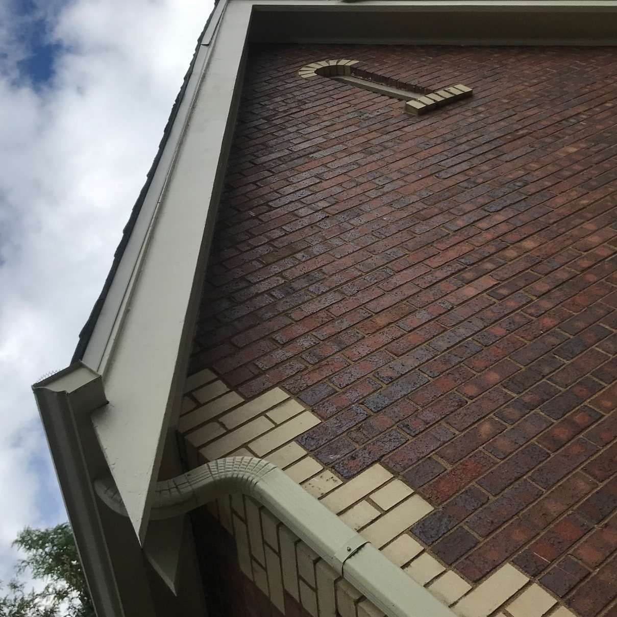 Red brick exterior of a building with light-colored trim and a decorative brick design. Blue sky.