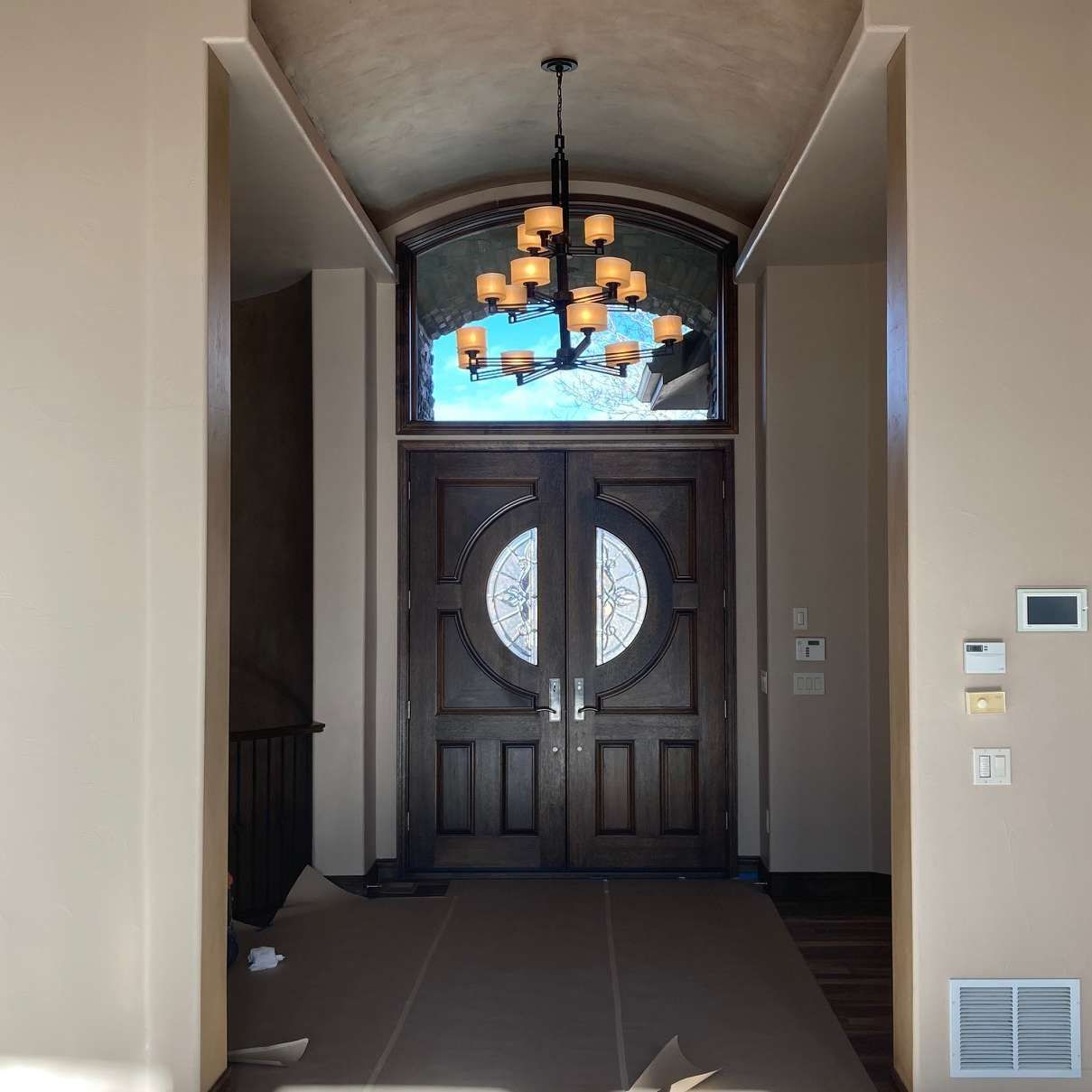 Brown double doors with decorative glass panels, topped by arched window and chandelier.