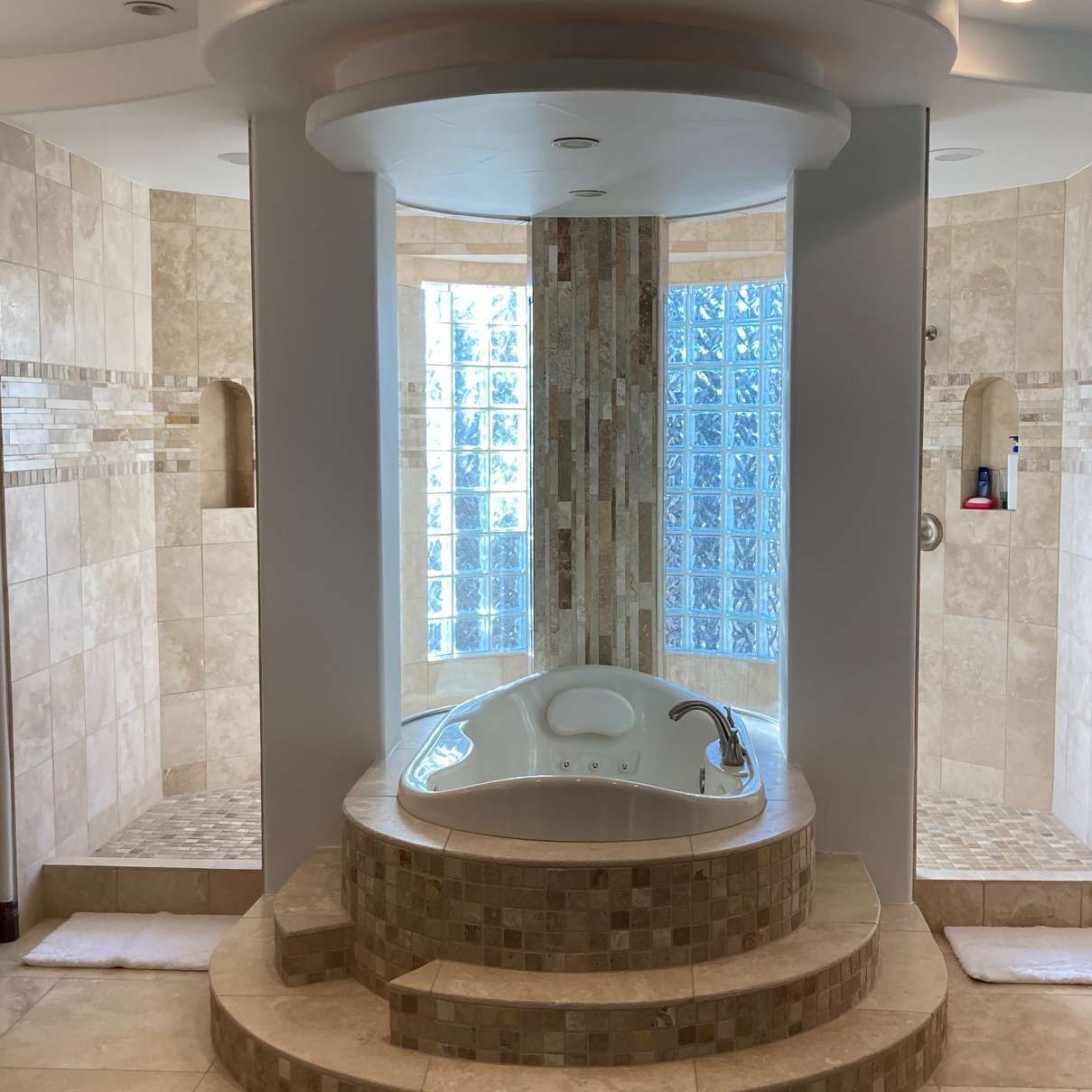 Luxurious bathroom with a sunken bathtub, two showers, and a window.