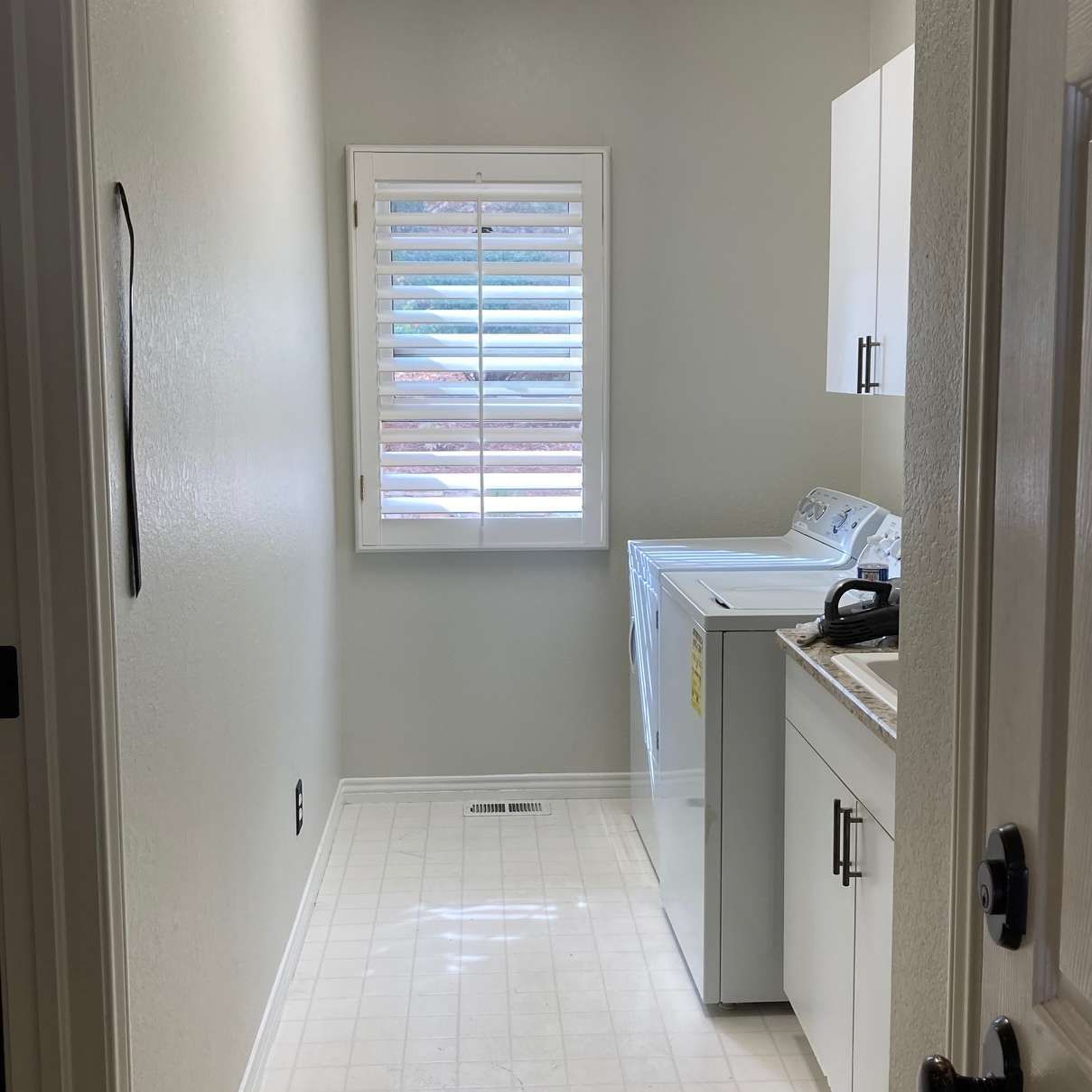 Laundry room: white appliances, cabinets, window with shutters, and light gray walls.
