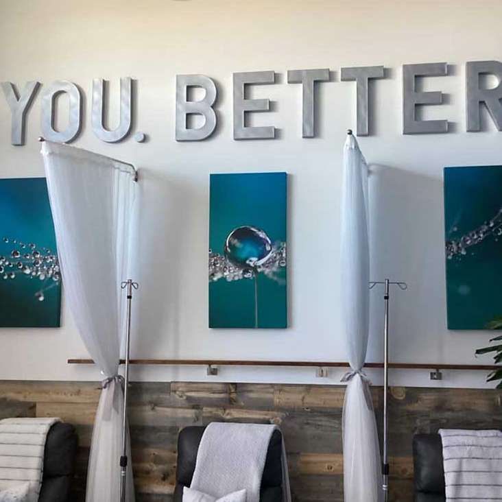 A medical spa with chairs, IV stands, curtains, art, and the words 