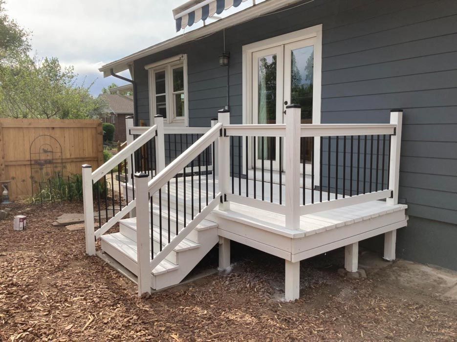 White deck with black railing and steps attached to a blue house, outside.