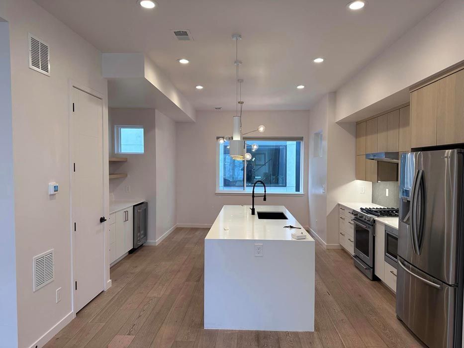 Modern kitchen with white island, stainless steel appliances, and light wood cabinets.