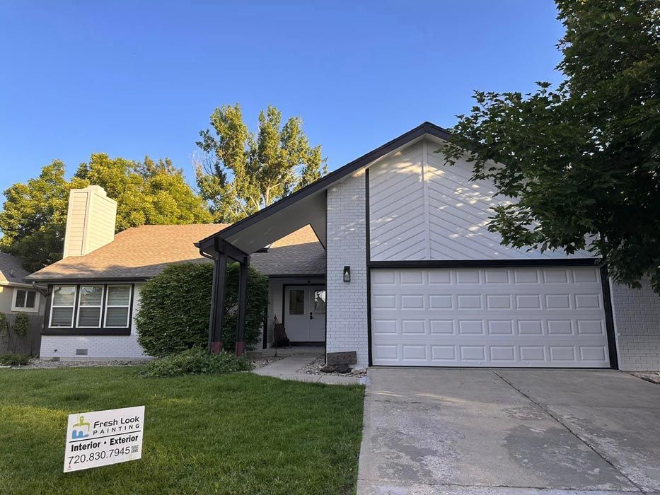A white house with black trim, a garage door, and a green lawn.