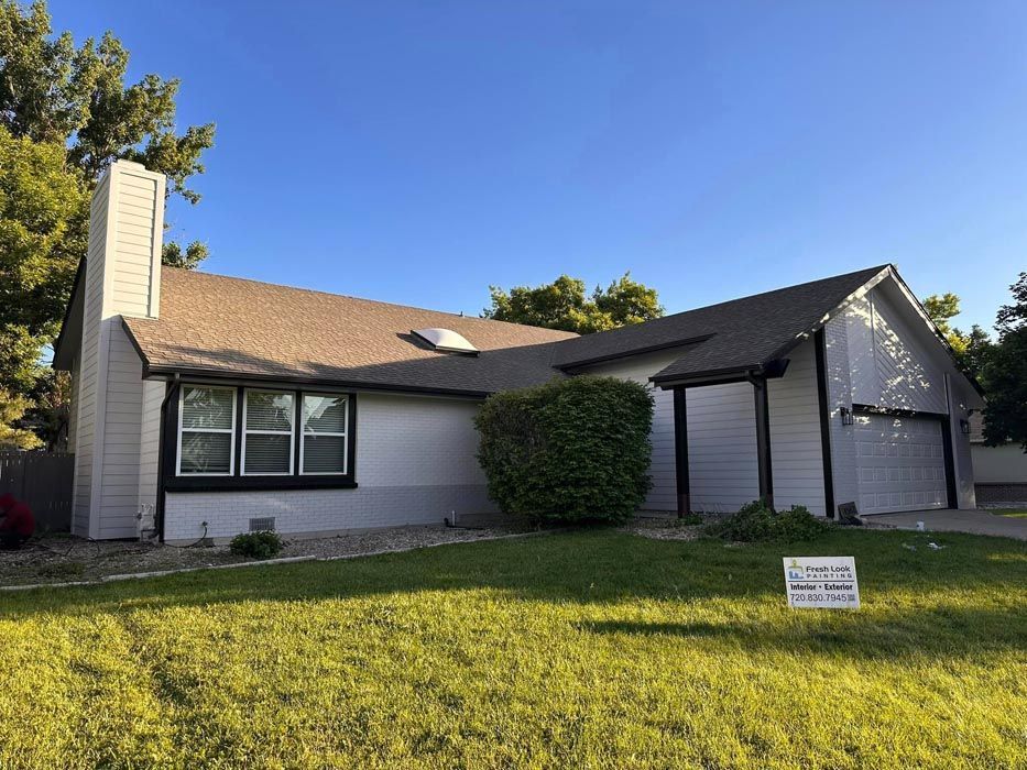 A gray house with a brown roof, green grass, and a blue sky in the background.