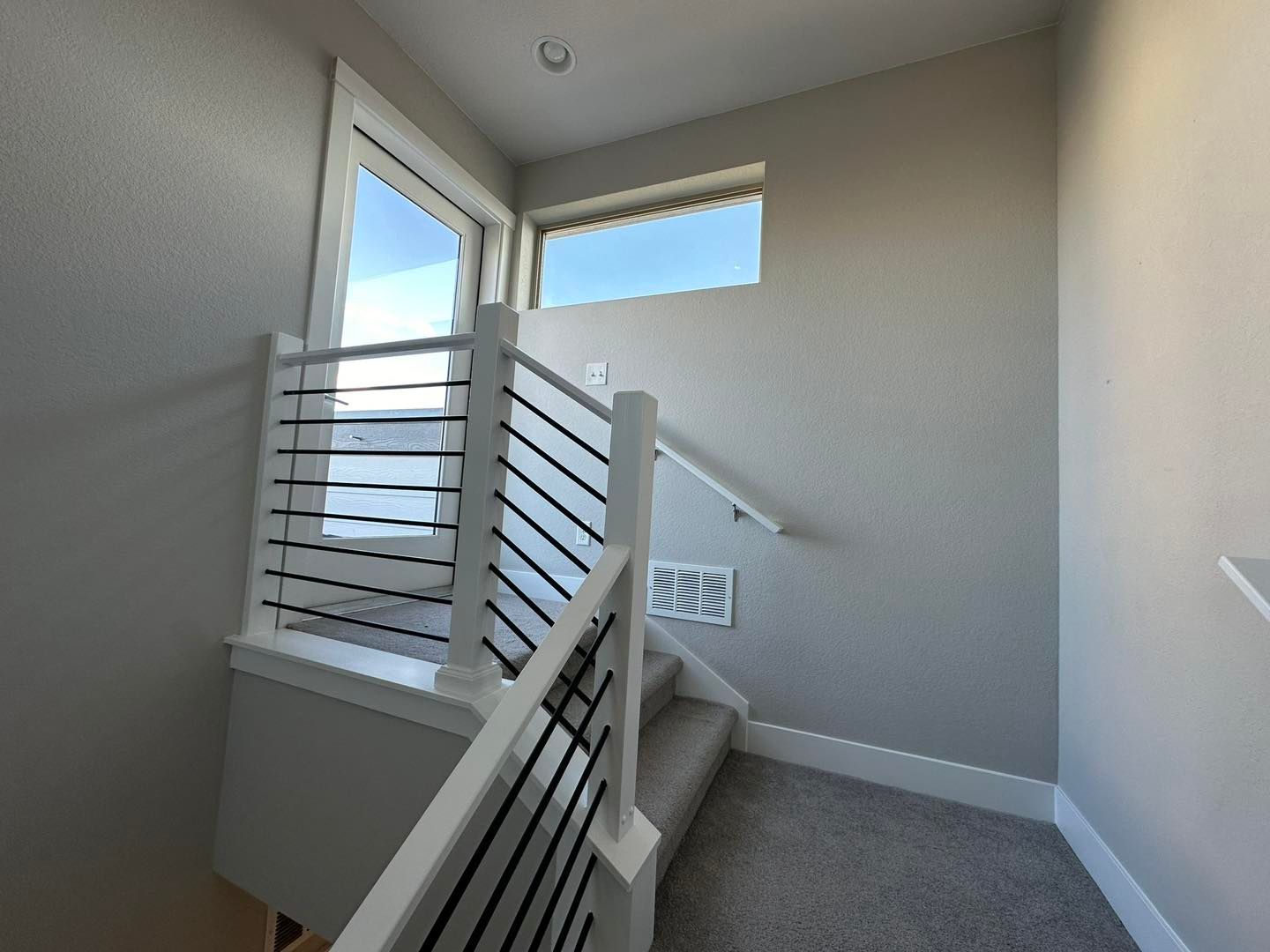 Staircase with white railing, black horizontal bars, carpeted steps, and window letting in natural light.