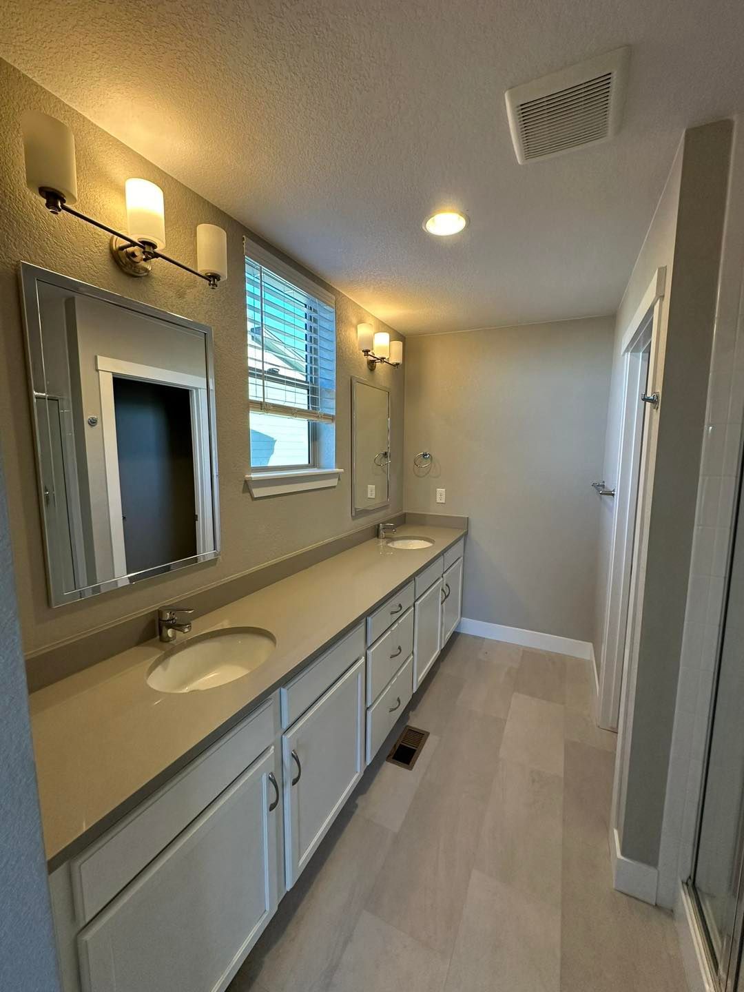 Bathroom with white cabinets, gray countertop, two sinks, and mirrors.