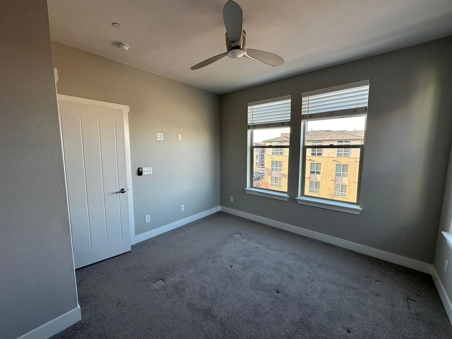 Empty room with gray walls, carpet, windows, and ceiling fan.