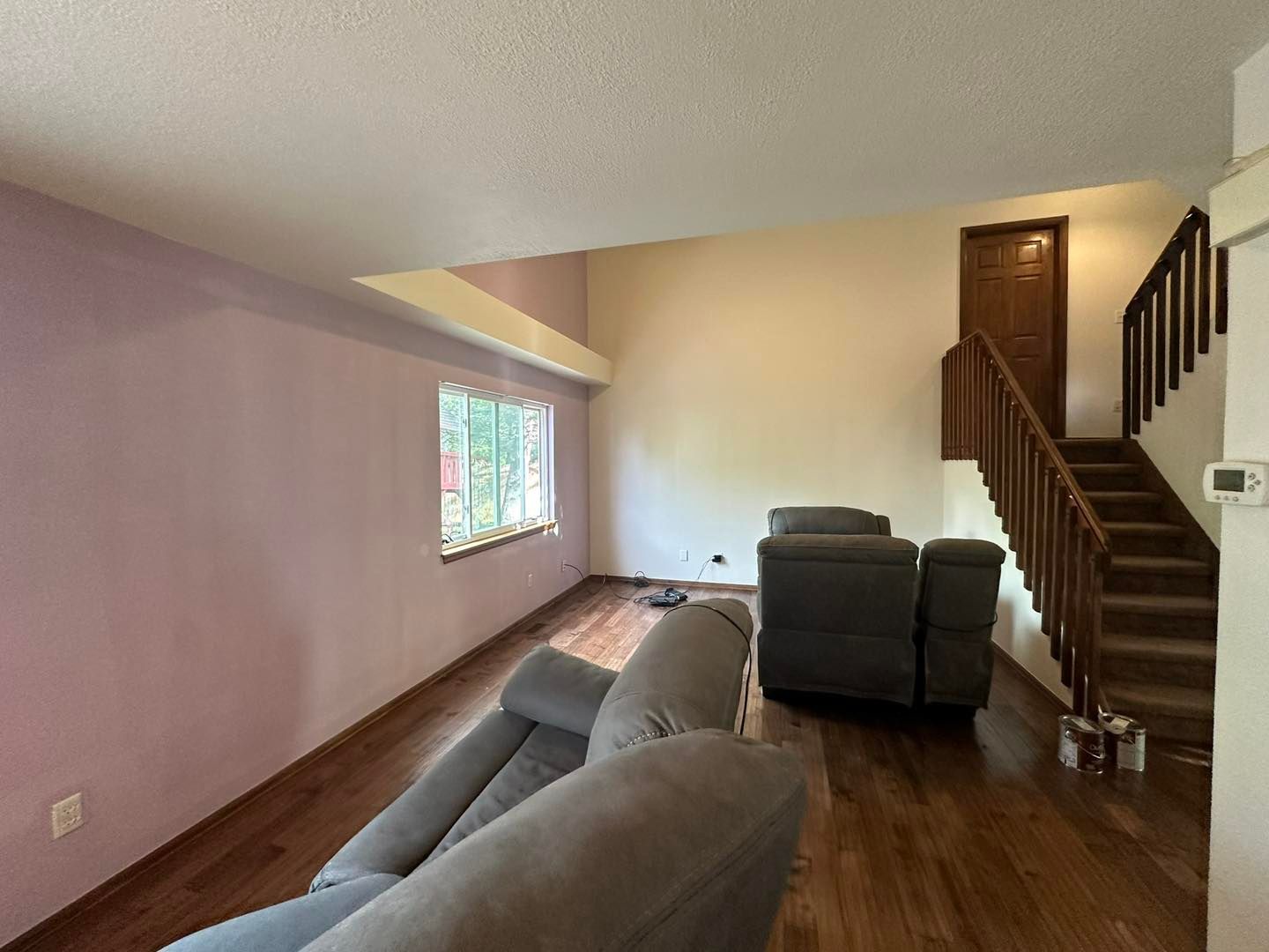 Living room with two gray recliners, wooden floor, and a staircase leading up. Pink and beige walls.