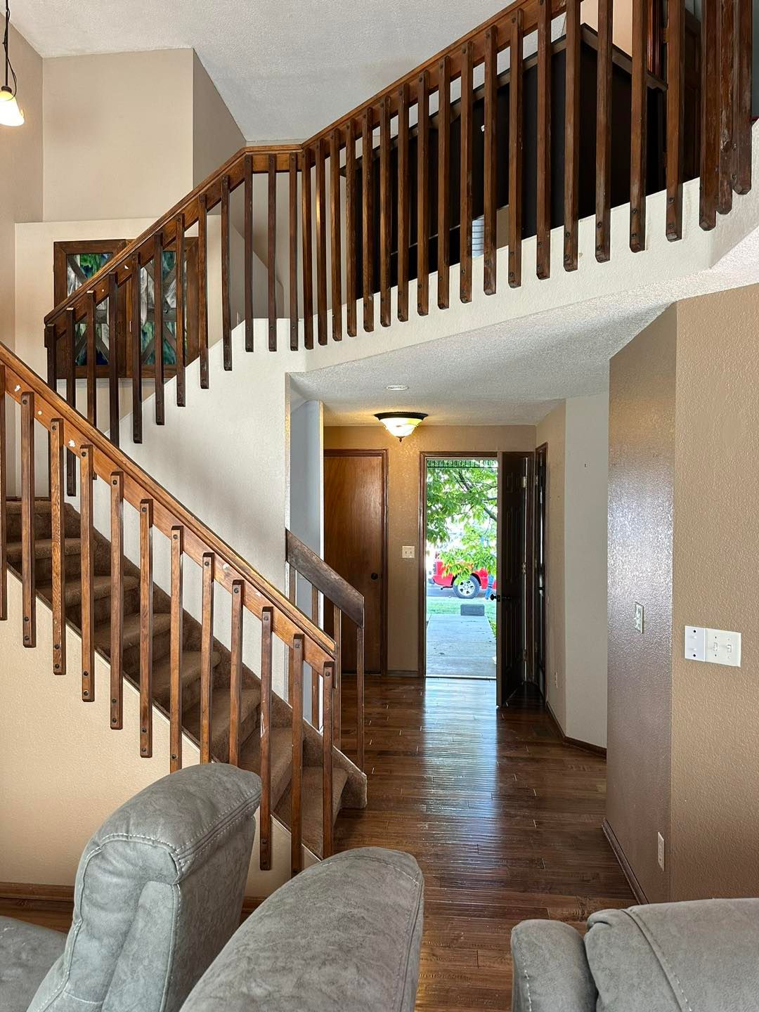 A two-story entryway with a staircase, wooden railing, and a view of an open door to the outdoors.