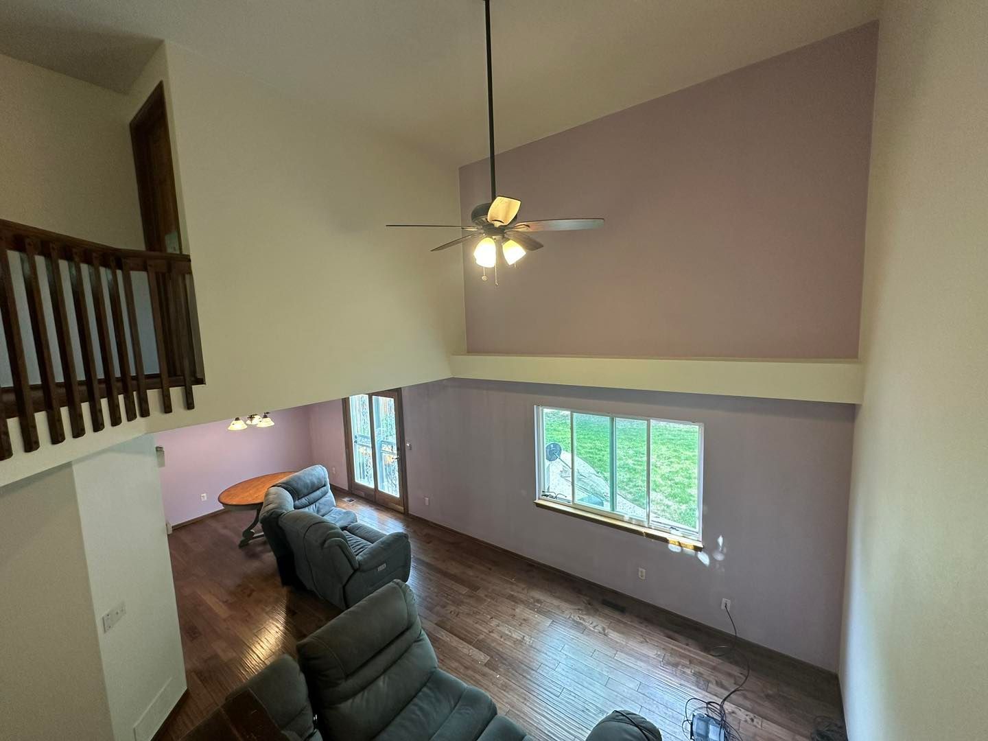High-angle interior view with a loft area, wood floors, two recliners, and purple accent walls.