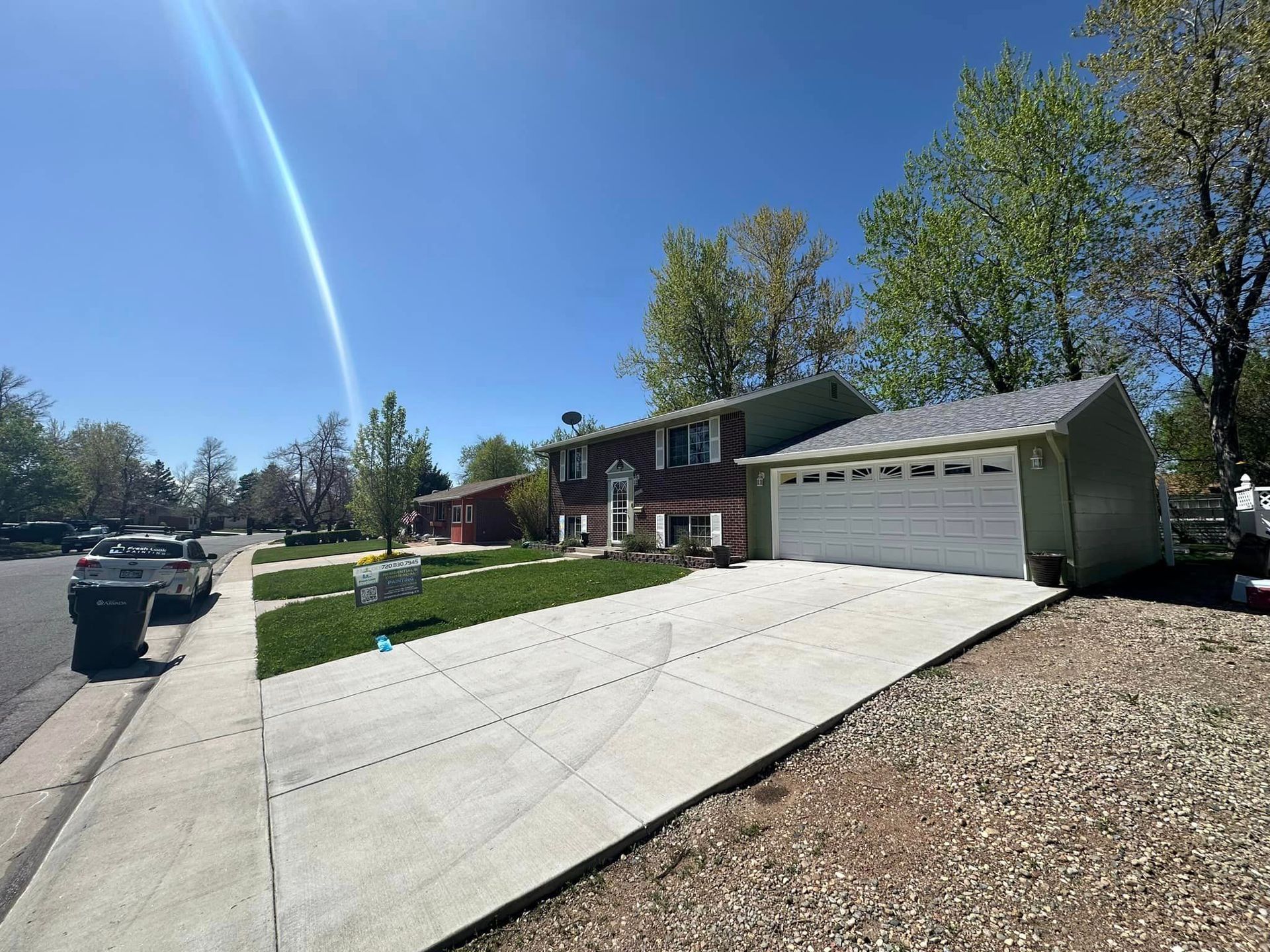 Two-story house with green siding, attached garage, and long driveway on a sunny day.