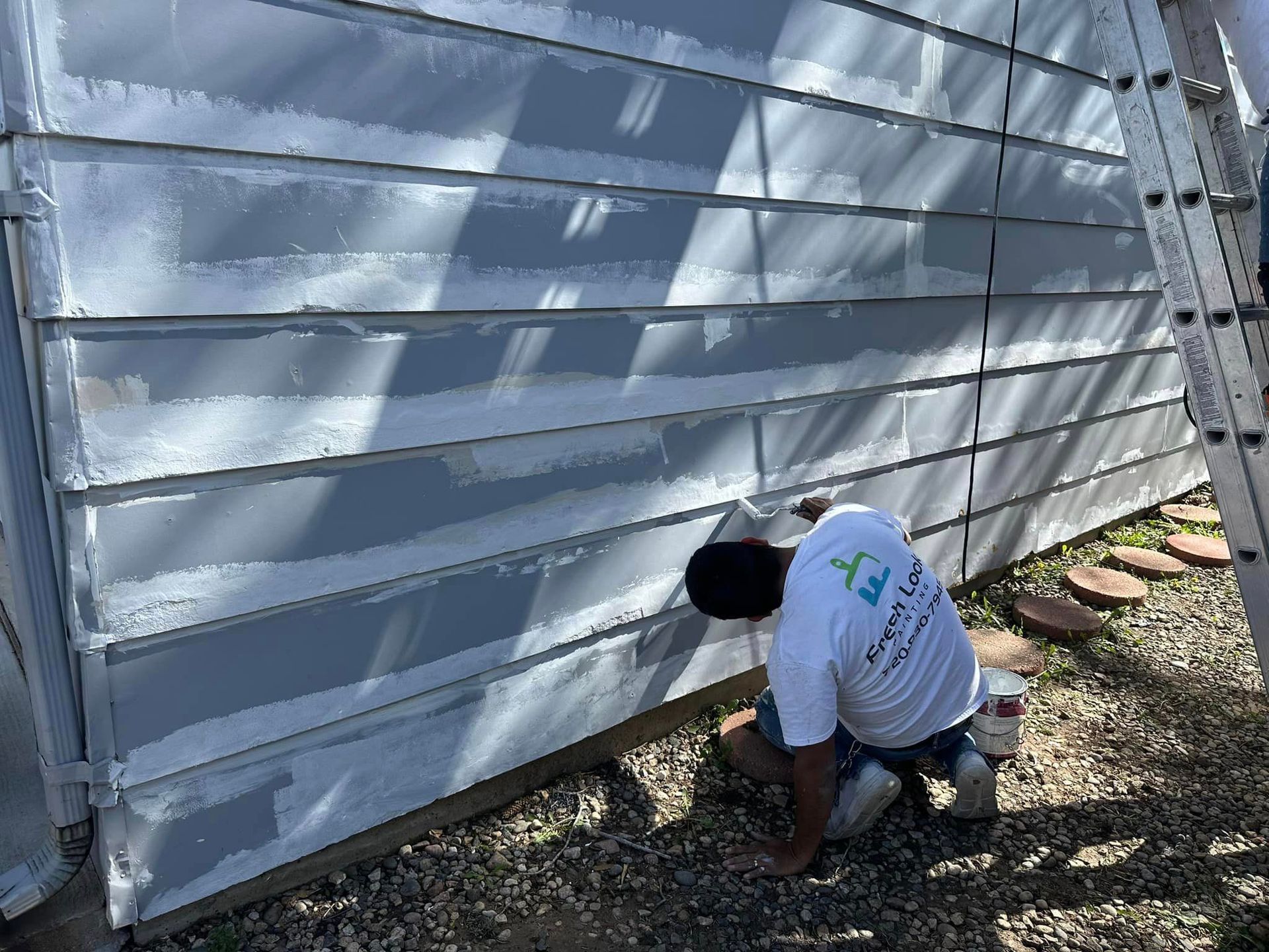 Person painting siding of a light gray house. Ladder on the right.