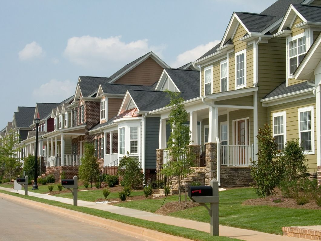 Row of colorful houses with front porches and black mailboxes along a sidewalk and grass on a sunny day.