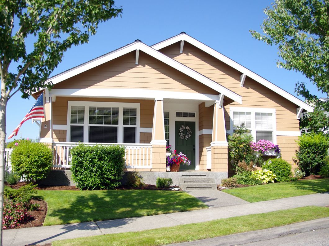 Tan craftsman-style house with green door, white trim, American flag, and well-kept lawn.