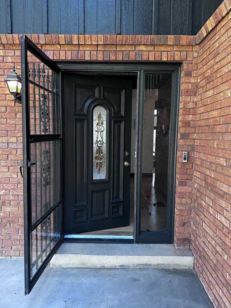 Black front door with open security screen and brick facade.
