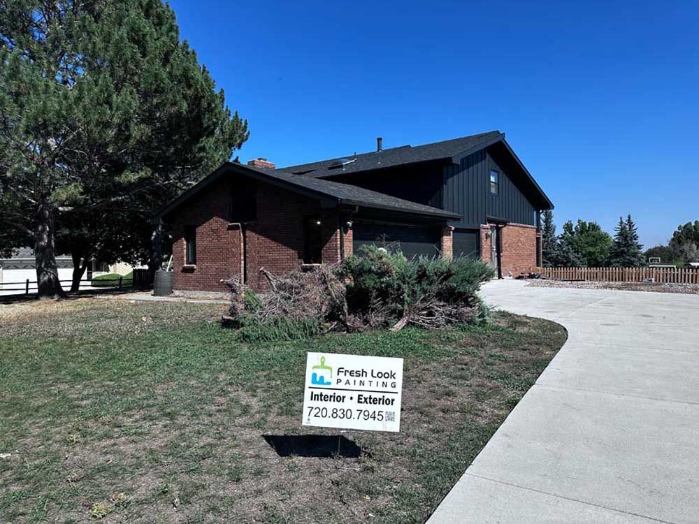 A house with brick facade and dark roof, sign in the foreground for 