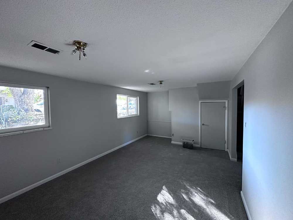 Empty room with gray carpet, walls, and a white ceiling, featuring two windows and a closed door.