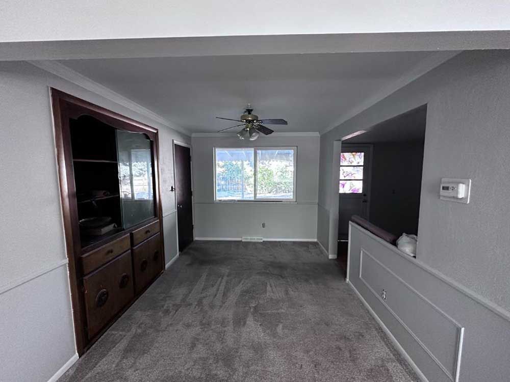Dining room interior with gray carpet, built-in cabinet, window, and doorway to another room.