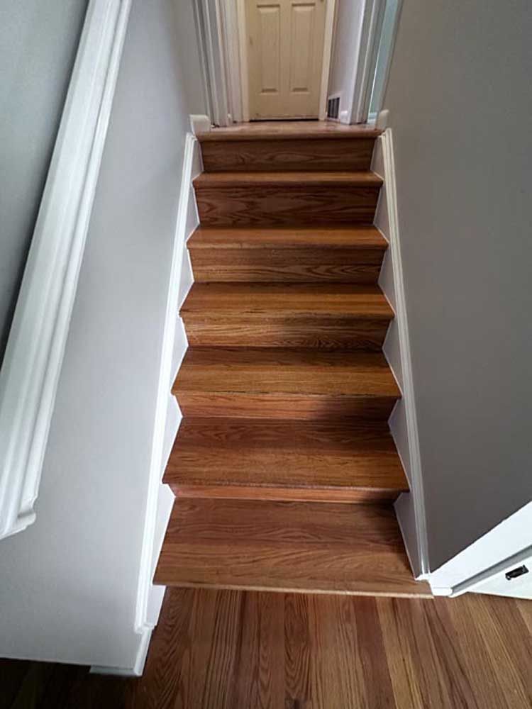 Wooden staircase with white trim and gray walls.