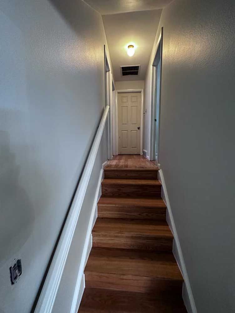 Staircase leading to a hallway with a closed door, white trim, and gray walls.