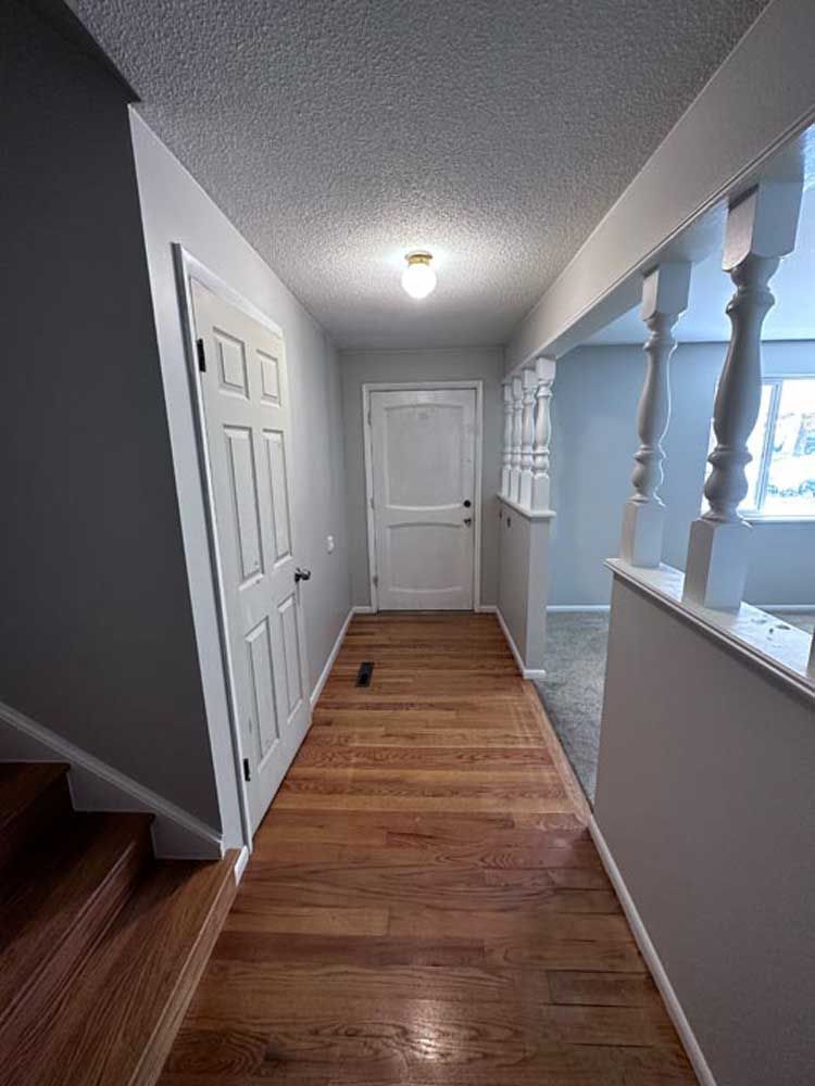 Hallway with hardwood floor, gray walls, white doors, and staircase.