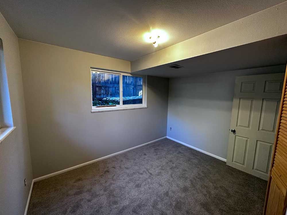 Empty room with a window, gray walls, carpet, and a closed door.
