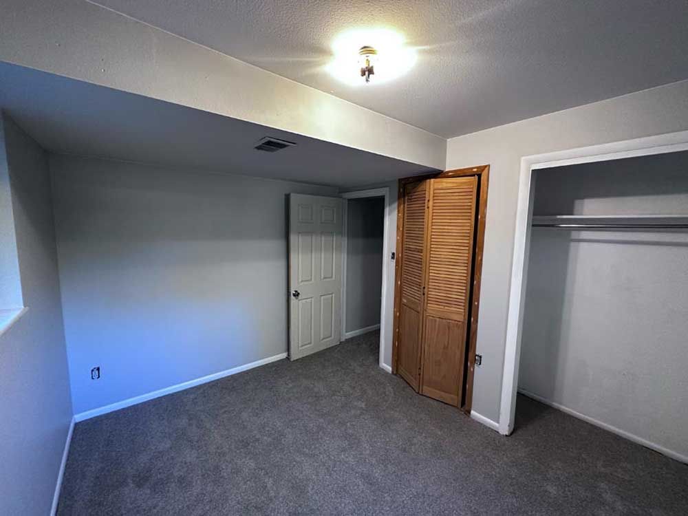 Empty gray-walled bedroom with carpet, closet, wooden bi-fold doors, and a closed door.