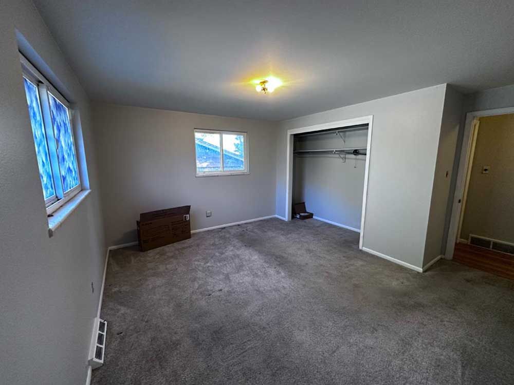 Empty bedroom with gray walls, carpet, window, and closet.