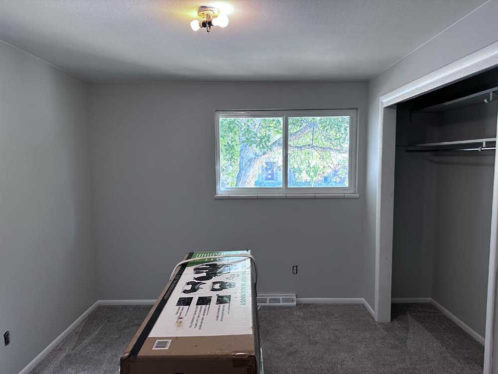 Empty bedroom with gray walls, carpet, window, and closet. A cardboard box sits in the center.