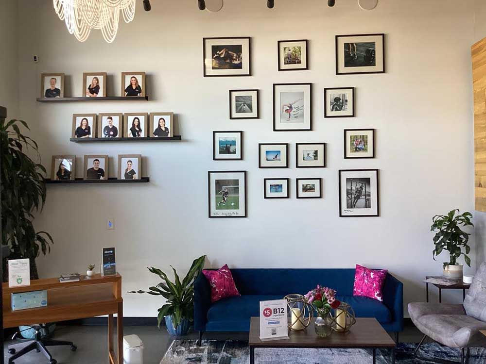 A waiting area with a blue couch, a gallery wall of framed art, and framed headshots on shelves.