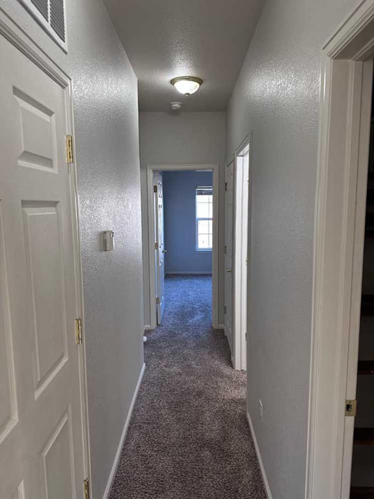 Narrow hallway with gray walls, carpet, and white doors leading to rooms.