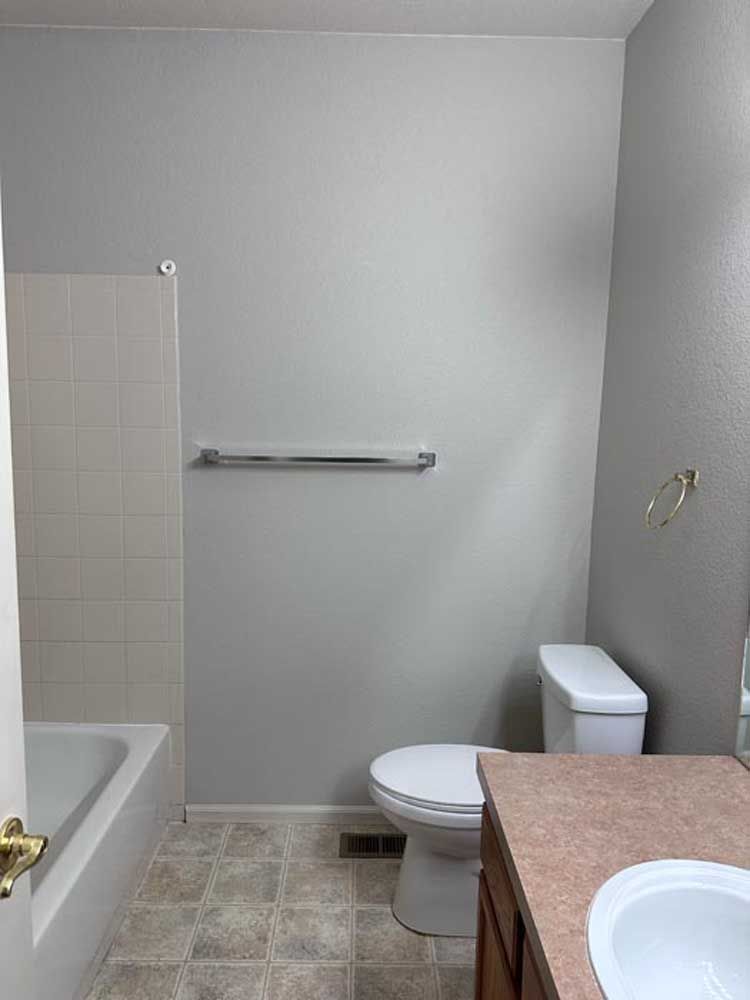 A small bathroom with a toilet, sink, tub, and towel rack, painted in gray and white.