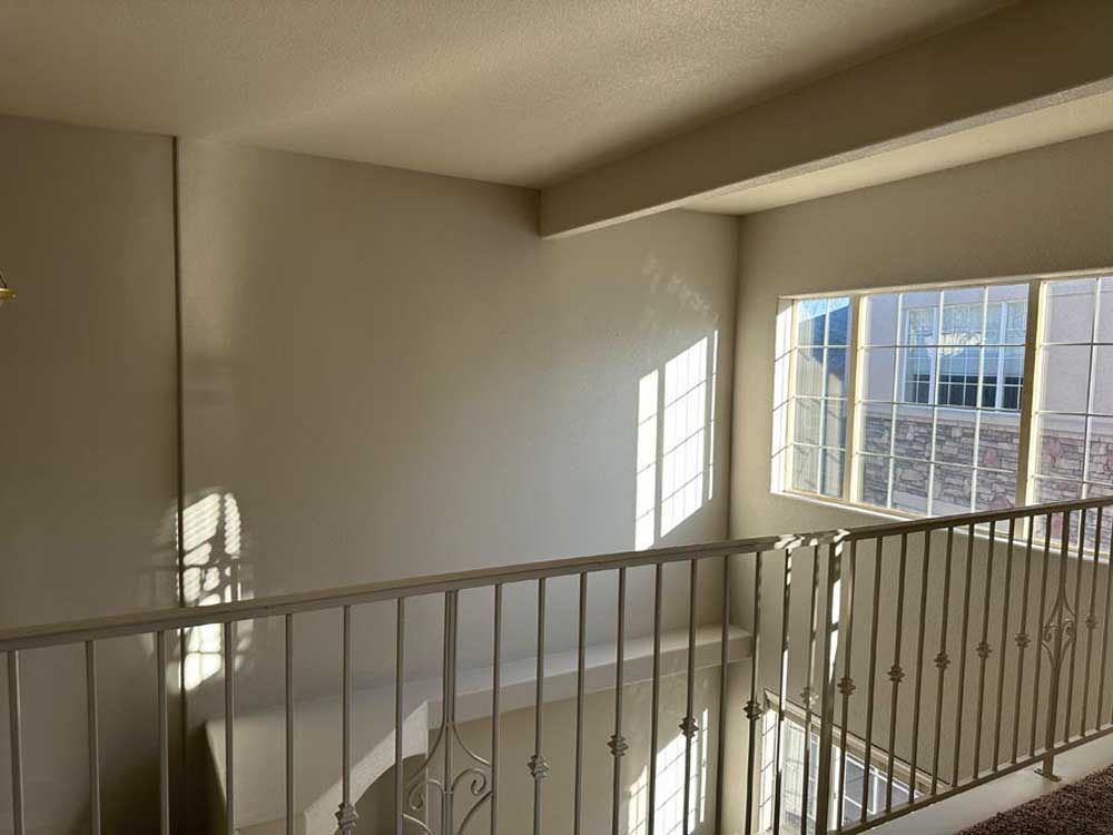 Interior view of a balcony overlooking a lower level, with a large window and metal railing.