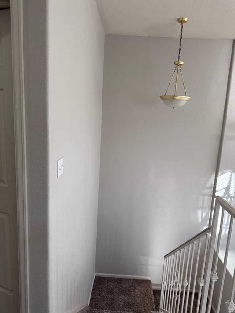 Hallway with light fixture, staircase, and door. Gray walls and carpet.