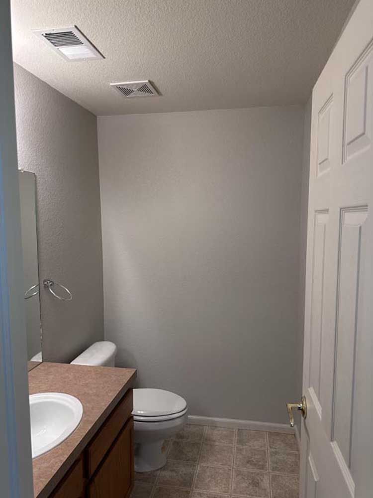 A small bathroom with gray walls, a toilet, sink, and closed white door.