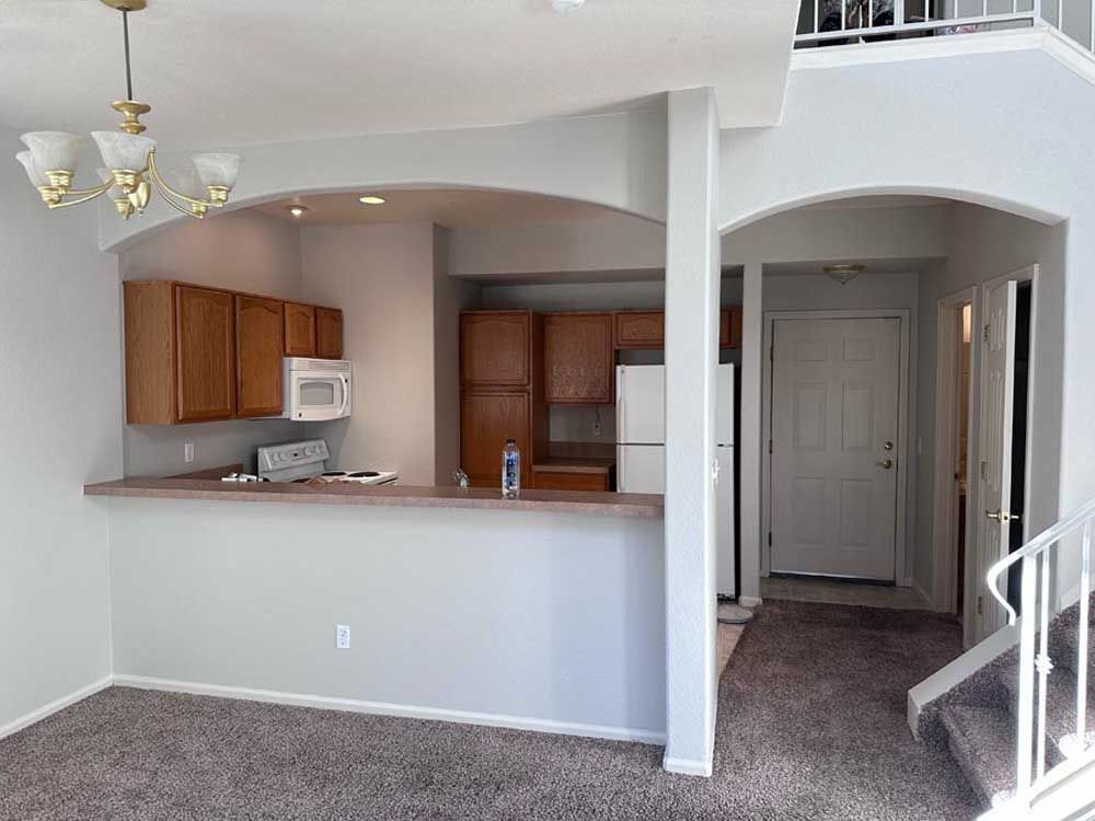 Interior view of a kitchen with light-colored cabinets, a bar, and an entrance. Brown carpet and white walls.