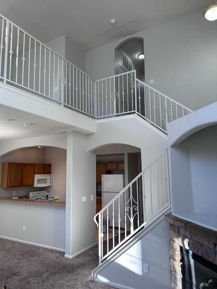 Two-story interior with staircase and balcony featuring white railings. View includes kitchen and arched doorways.