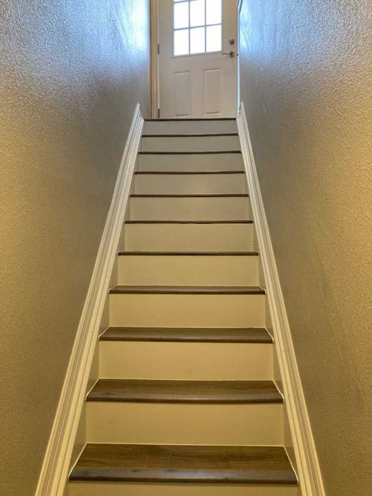 Staircase leading up to a white door, brown treads, white risers and trim, flanked by tan walls.