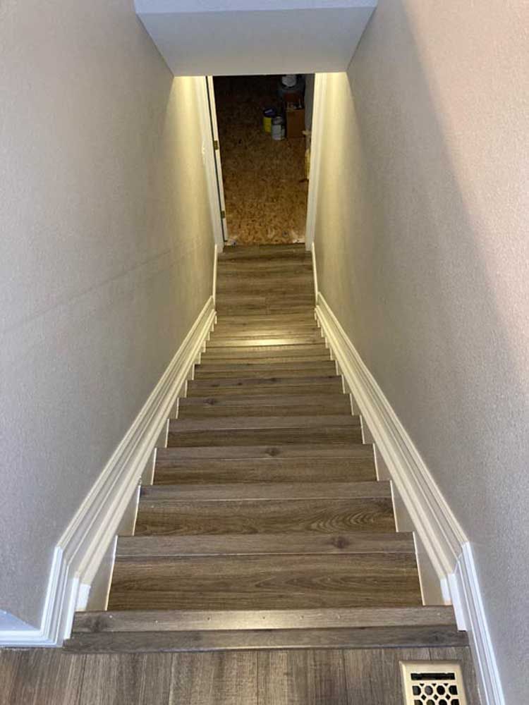 Wooden staircase leading down into a basement, flanked by light gray walls and white trim.
