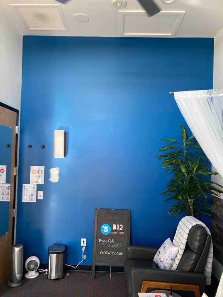 Blue wall in a waiting area with a black chair, sign, and plant.