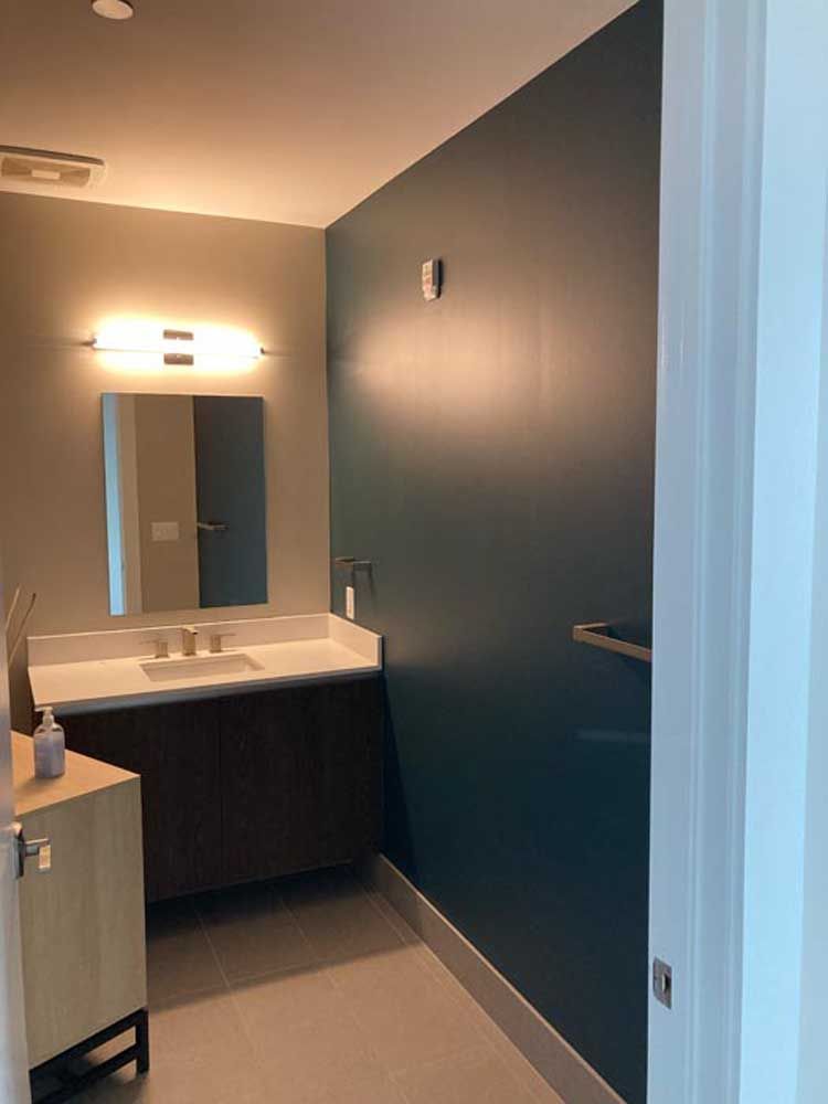 A modern bathroom with a dark blue wall, light vanity, and neutral gray floor.