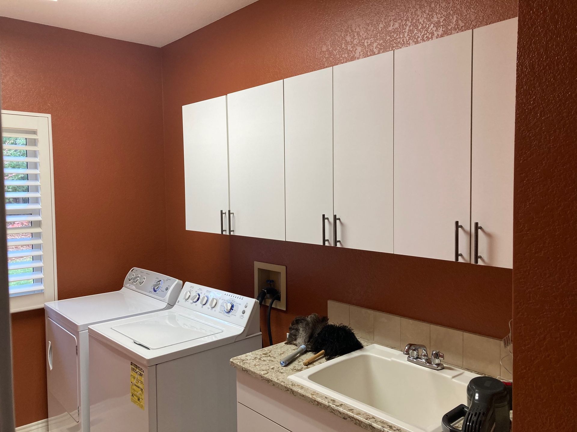 Laundry room with white cabinets, appliances, and a sink against orange walls.