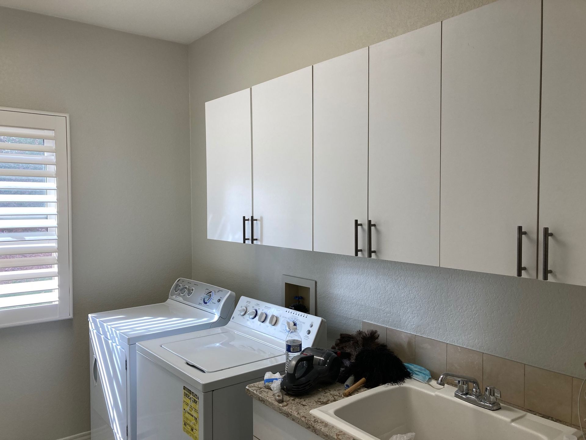 Laundry room with white cabinets over a washer, dryer, and utility sink.