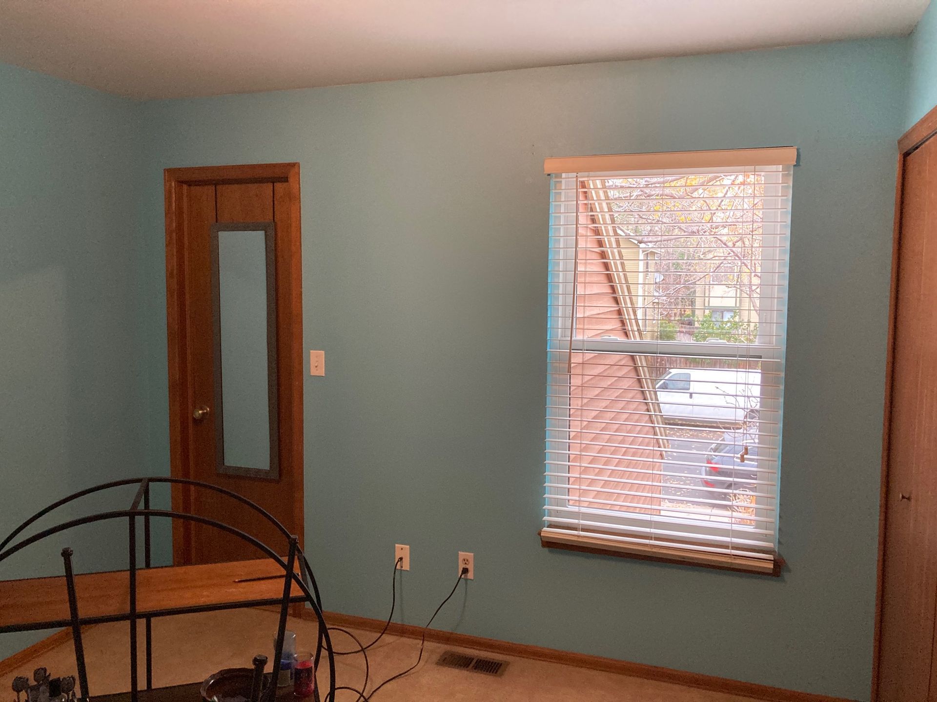 Room with teal walls, a wooden door with a glass panel, and a window with blinds.