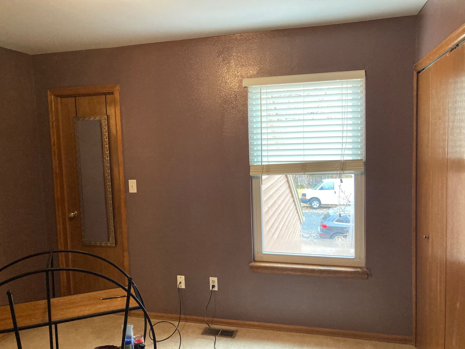 Bedroom with purple walls, wooden door, window with blinds, and a metal bed frame.