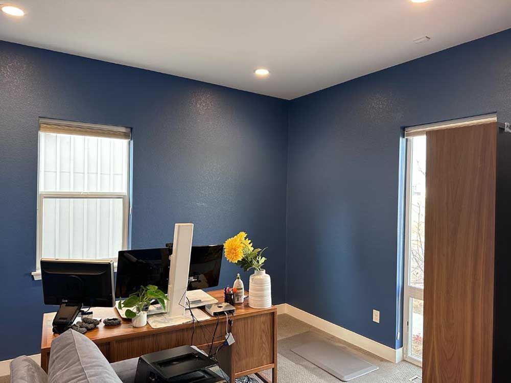 Office space with blue walls, a desk with monitors, and a window.