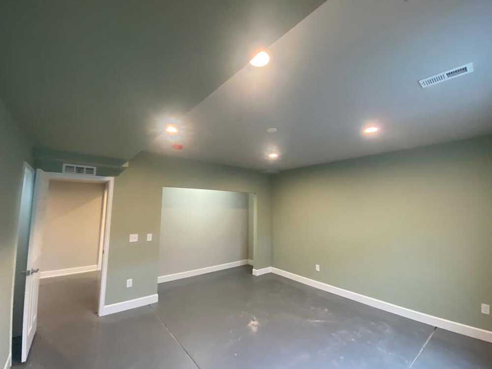 Empty room with green walls and gray floor, recessed lighting, and a doorway.